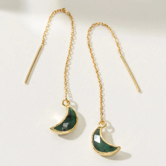 Gold earrings with green crescent moon charms on a light background