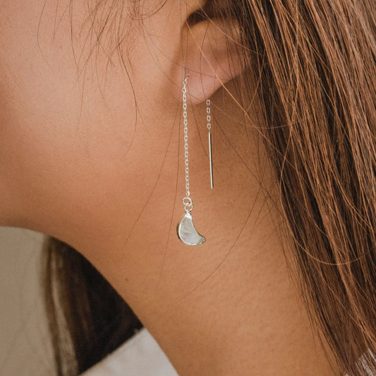 Silver earring with a moon pendant worn by a person with brown hair.