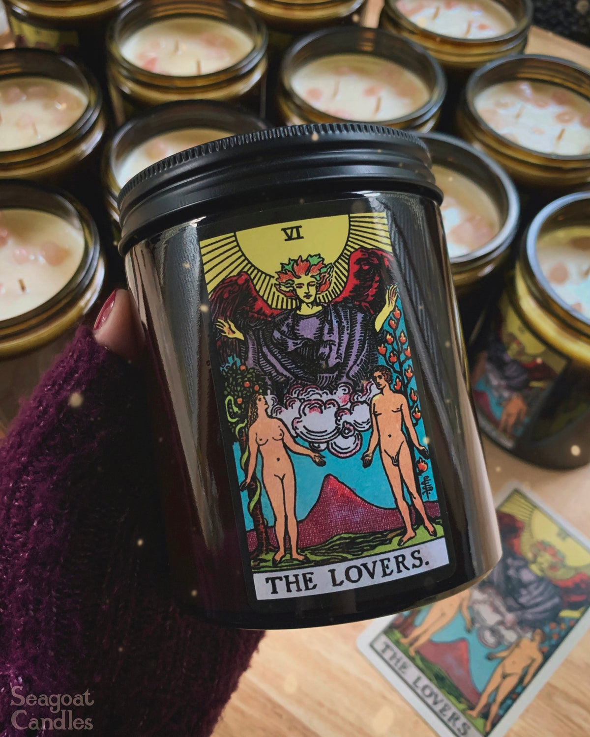 Candle jar with 'The Lovers' tarot card design held by a hand, surrounded by more candles and tarot cards.