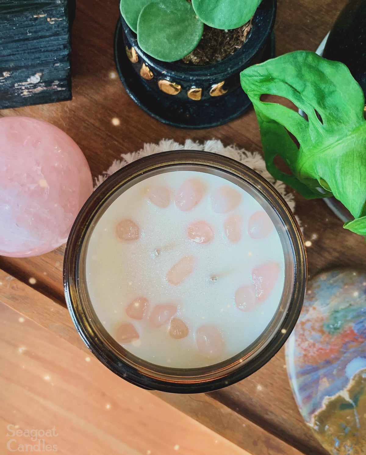 Candle with decorative stones on a wooden surface with plants and crystals.